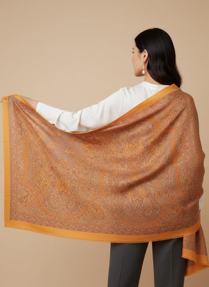 Woman wearing an saffron gold yellow pure wool hand embroidered kani jamawar shawl with intricate patterns  on a beige background