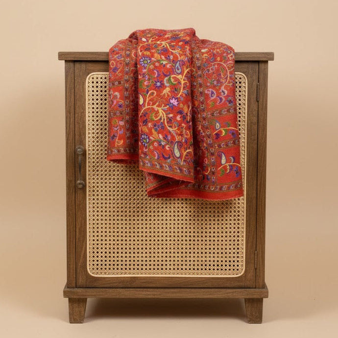 Wooden cabinet with a caned door featuring a red floral patterned paisley kalamkari-inspired stole in faux pashmina on a beige background