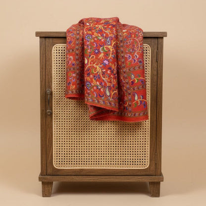 Wooden cabinet with a caned door featuring a red floral patterned paisley kalamkari-inspired stole in faux pashmina on a beige background