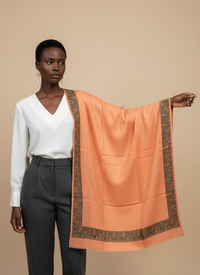 Woman holding a peach pashmina shawl with a patterned border against a beige background