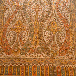 Close-up of a patterned fabric with intricate designs in brown, orange, and beige.