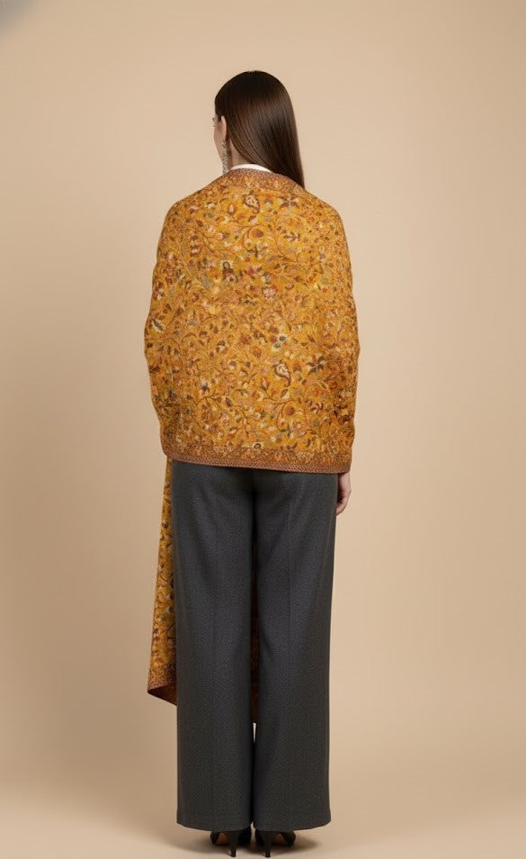 Person wearing a patterned mustard-colored Yellow floral patterned kani design shawl and dark pants on a beige background