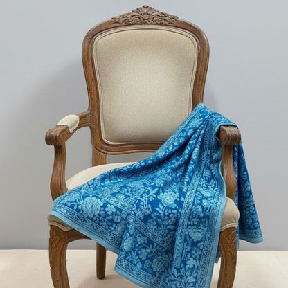Blue floral-patterned pashmina shawl draped over a wooden chair with a gray background